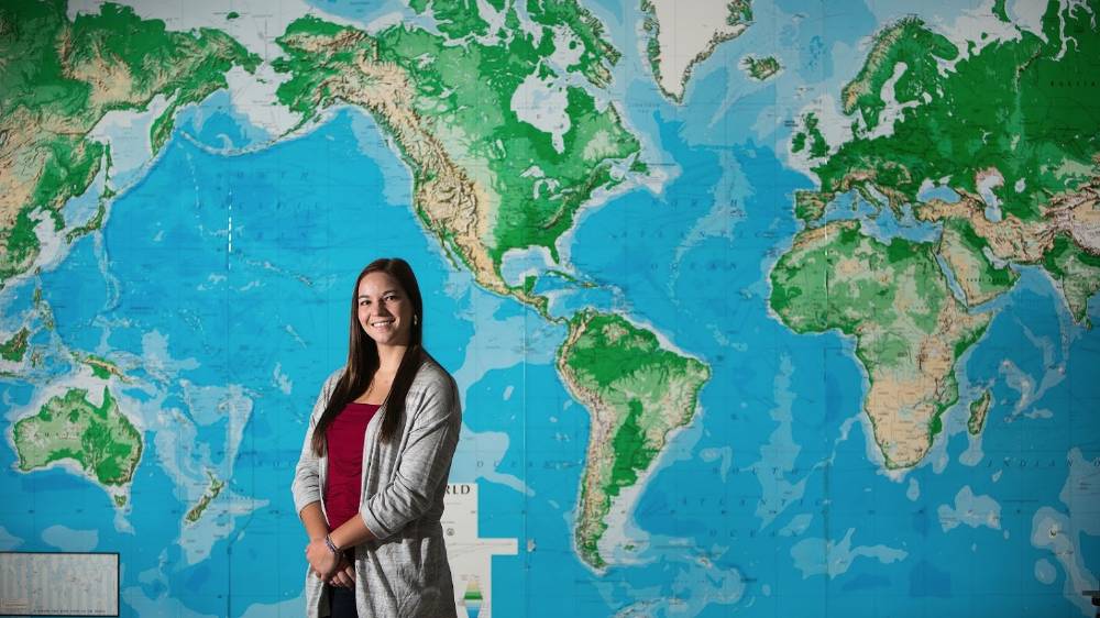 A international student poses in front of a map.